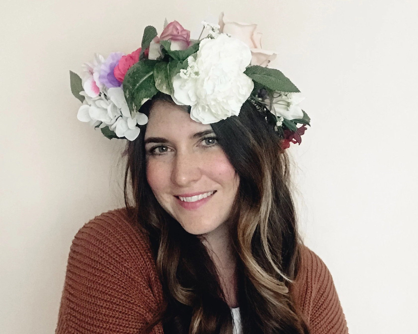 A woman in a brown cardigan with long brown hair is wearing a large floral crown on her head
