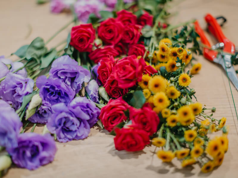 A selection of red, purple and yellow flowers lie on a wooden table