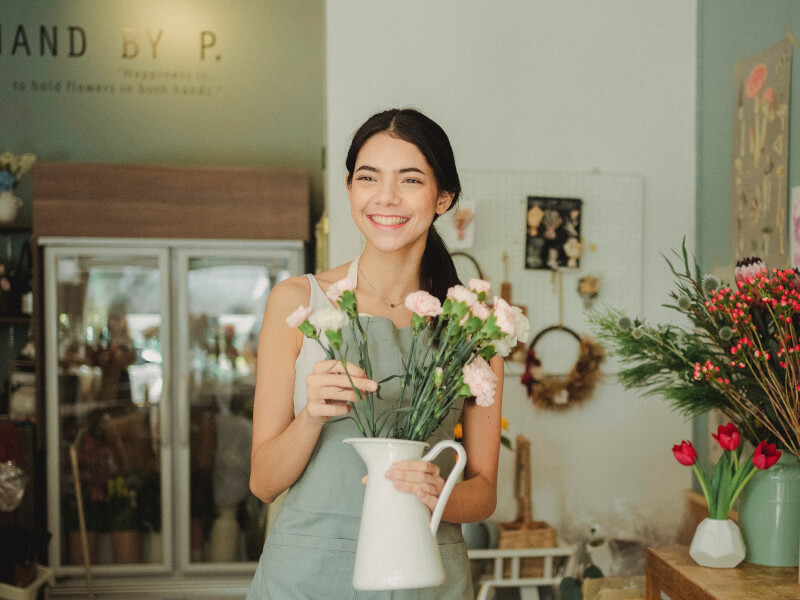 A person smiling whilst holding a vase containing a floral arrangement