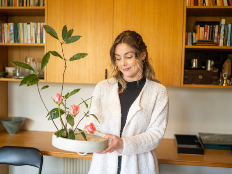 A woman is holding an ikebana flower arrangement made of pink roses 