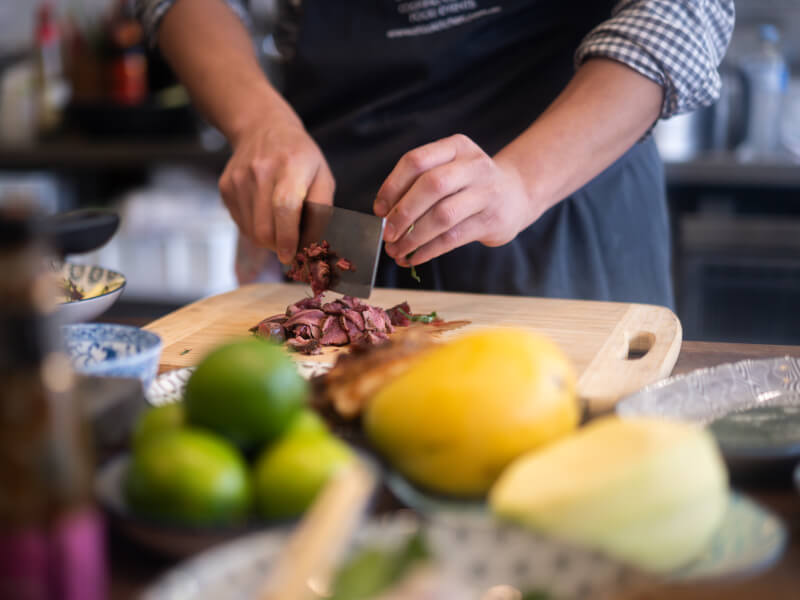 A close up of a person slicing cooked meat on a wooden chopping board, surrounded by smaller bowls