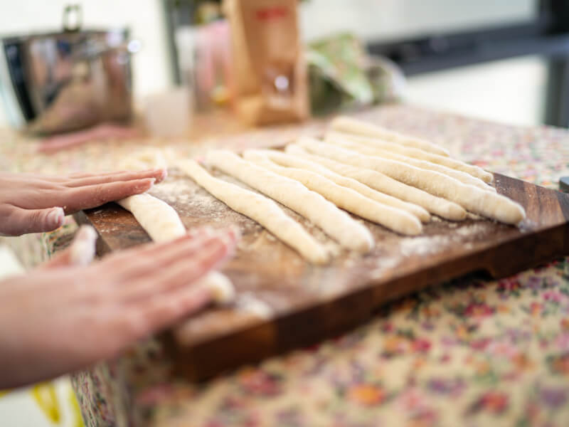 A close up of a person rolling out gnocchi dough on a wooden board