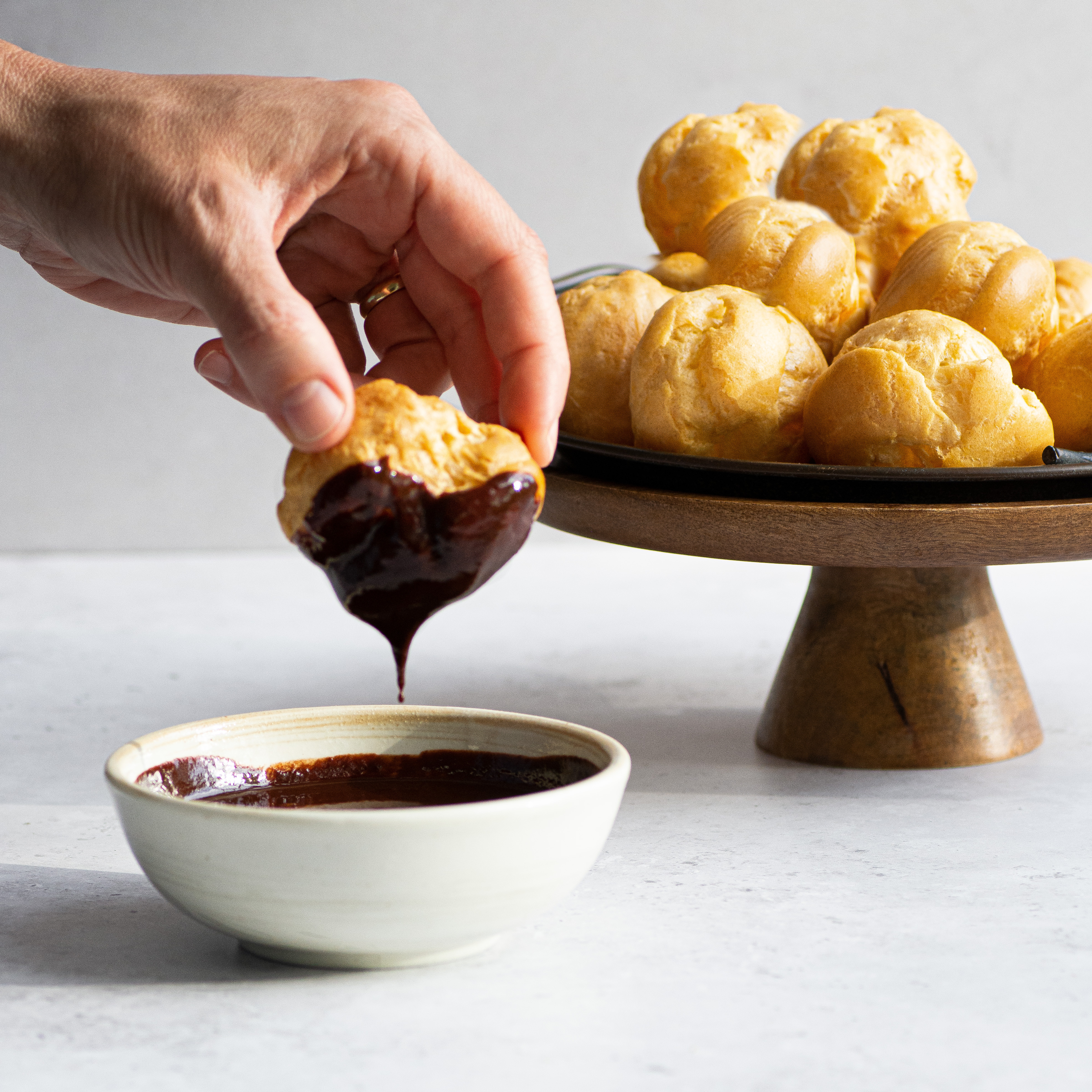 Close up of a hand dipping profiteroles into melted chocolate