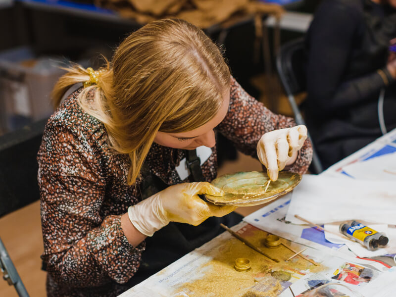 A woman at a Kintsugi class is repairing broken pottery with gold resin