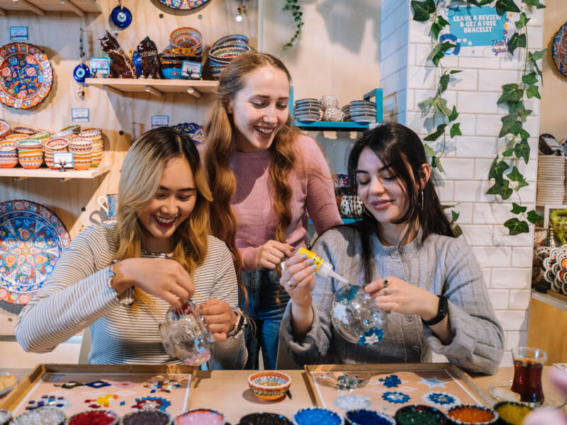 Two women are smiling and making mosaic glass lamps at a craft class