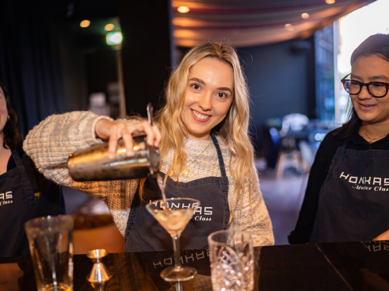 Three women are making cocktails and smiling at a cocktail making workshop