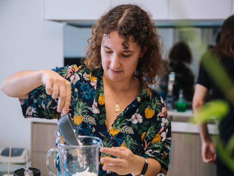 A woman is adding wax pellets to a large jar at a candle making class