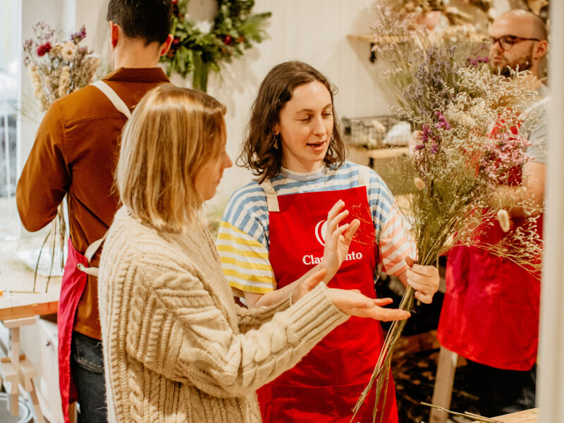 A teacher is showing a woman how to make a dried flower bouquet at a floristry class