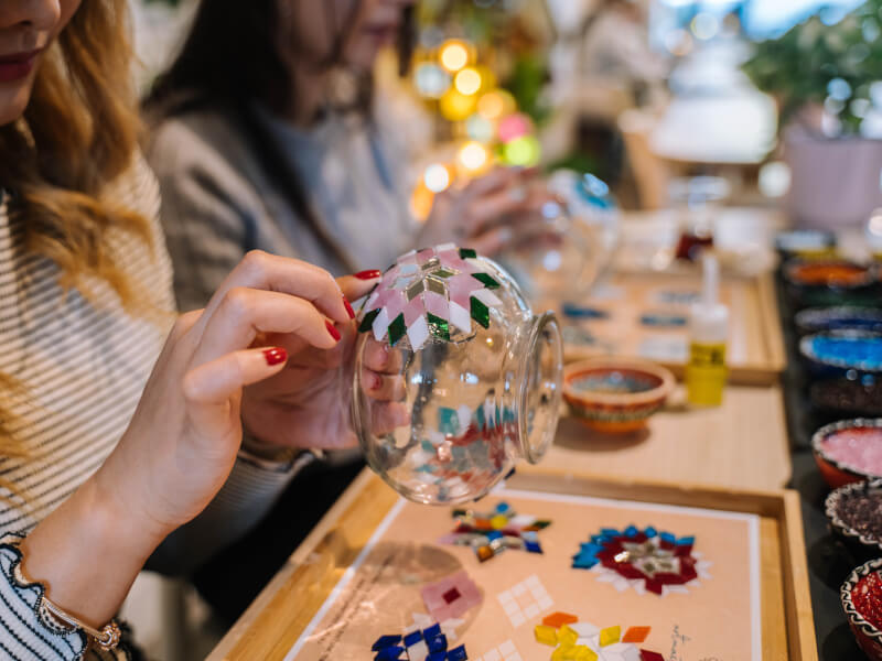 A person in a stripey top sits at a table holding a glass jar, which they're adding coloured diamond shaped tiles to
