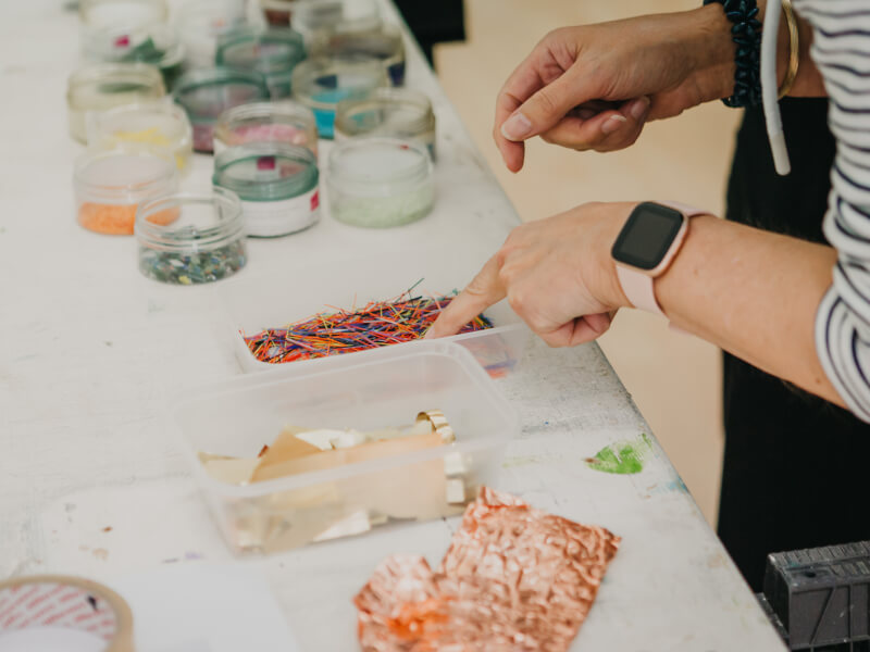 A close up image of someone at a mosaic workshop with various tubs of tiles on a table 