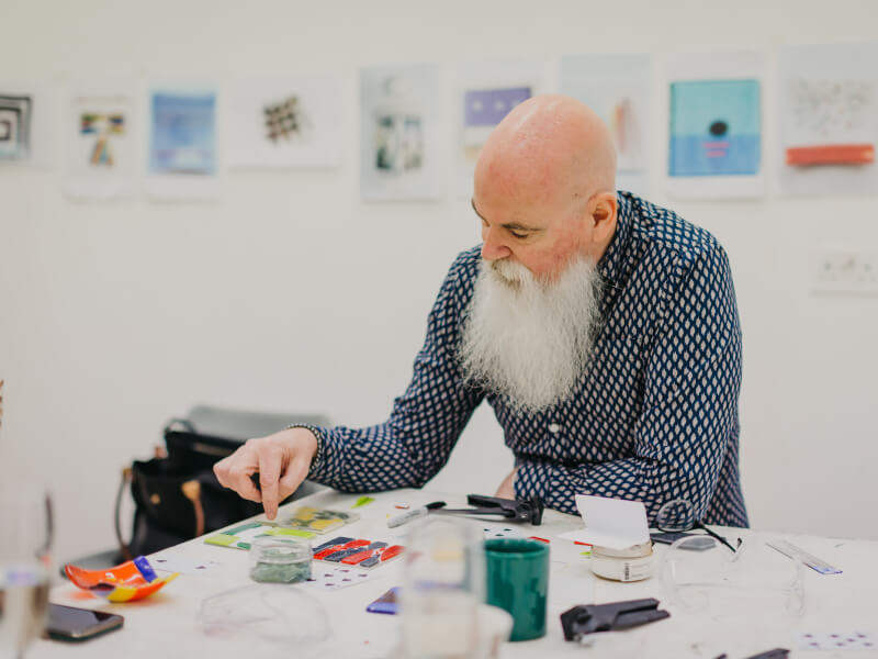 A man sits at a table with a simple red and blue mosaic design in front of him