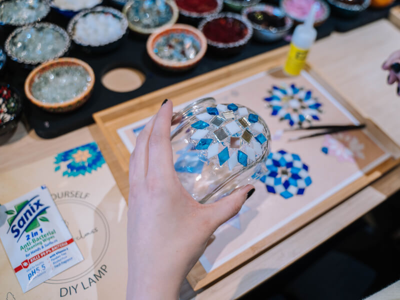 A person is making a blue and white mosaic on a glass jar