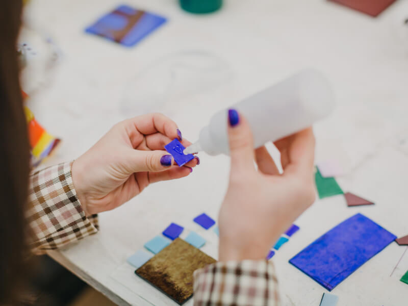 A close up of a person in a brown checked shirt adding glue to a small blue mosaic tile 