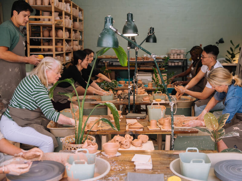 A group of people sit at pottery wheels at a ceramic class