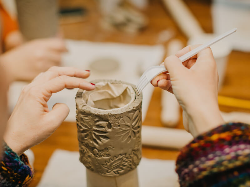 A close up of a person adding detail to a handmade clay mug
