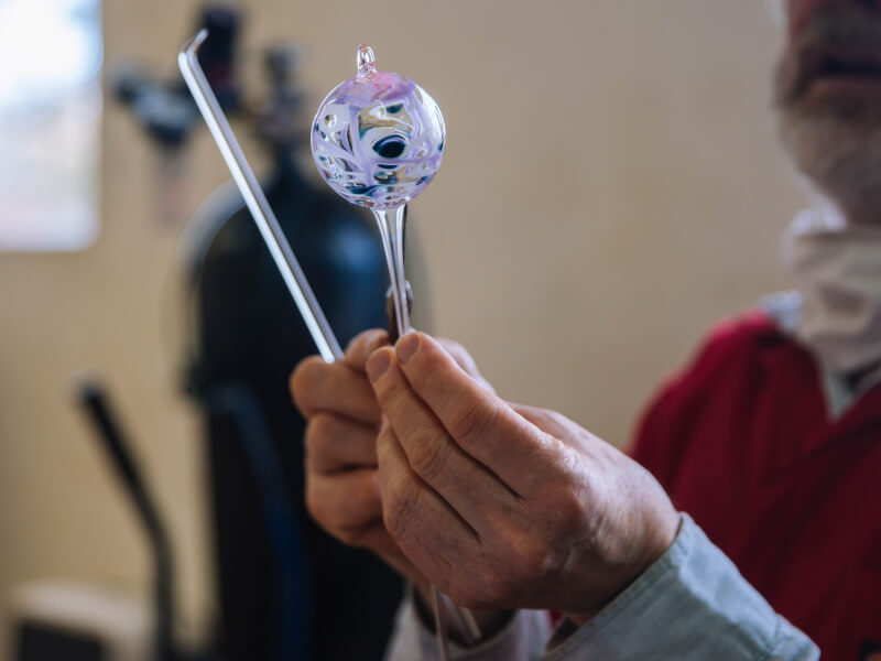 A person at a glassblowing class is holding a purple hand blown cylinder