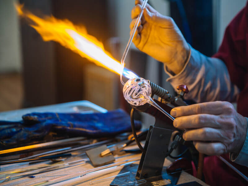 A close up of a person blowing molten glass into a sphere