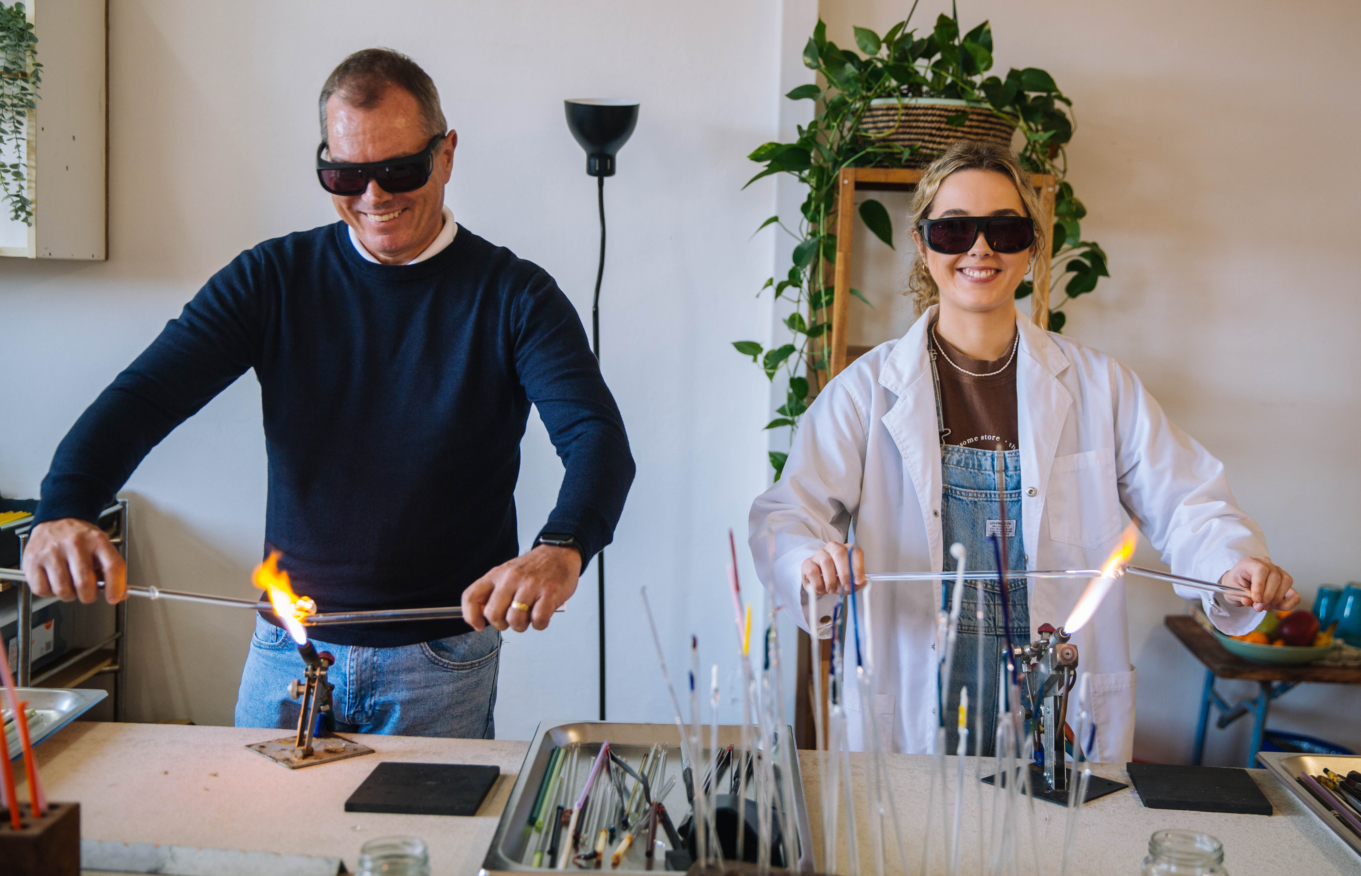 A man and woman are holding glass in molten flames to melt it at a glassblowing class