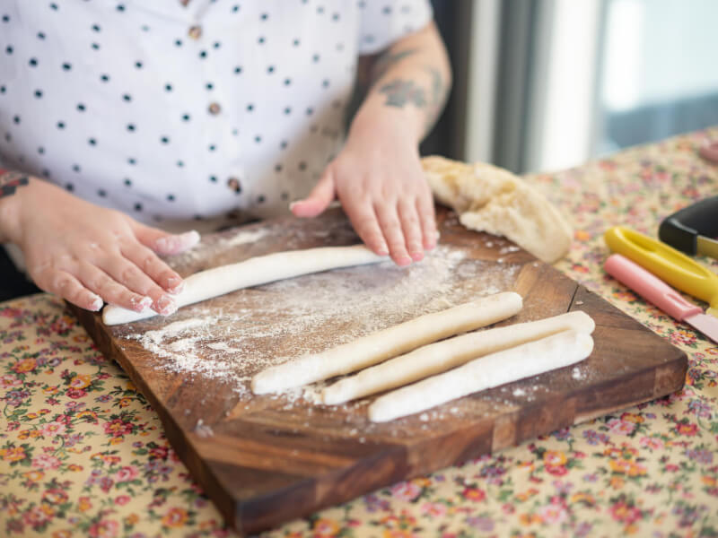 A close up of a persons hands rolling out gnocchi dough on a wooden board