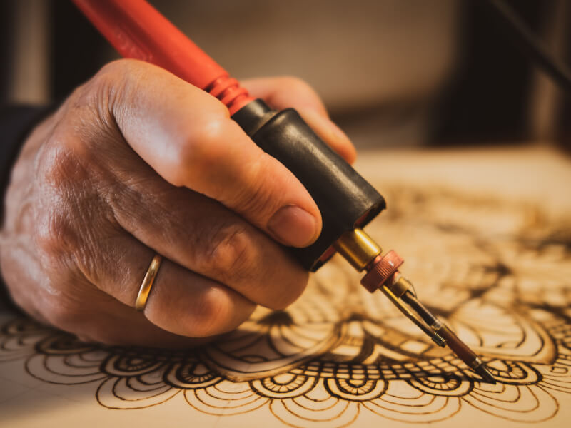 A person makes wood art using pyrography or wood burning.