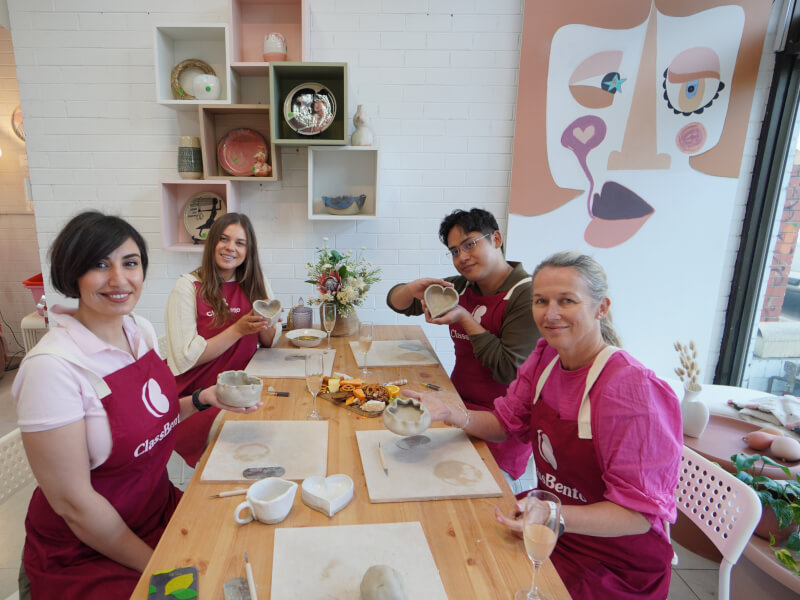 A group of four people are holding up their handmade pottery projects