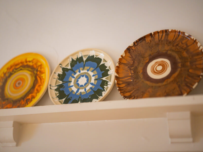 Three hand painted plates in vibrant colours and patterns sit on a shelf