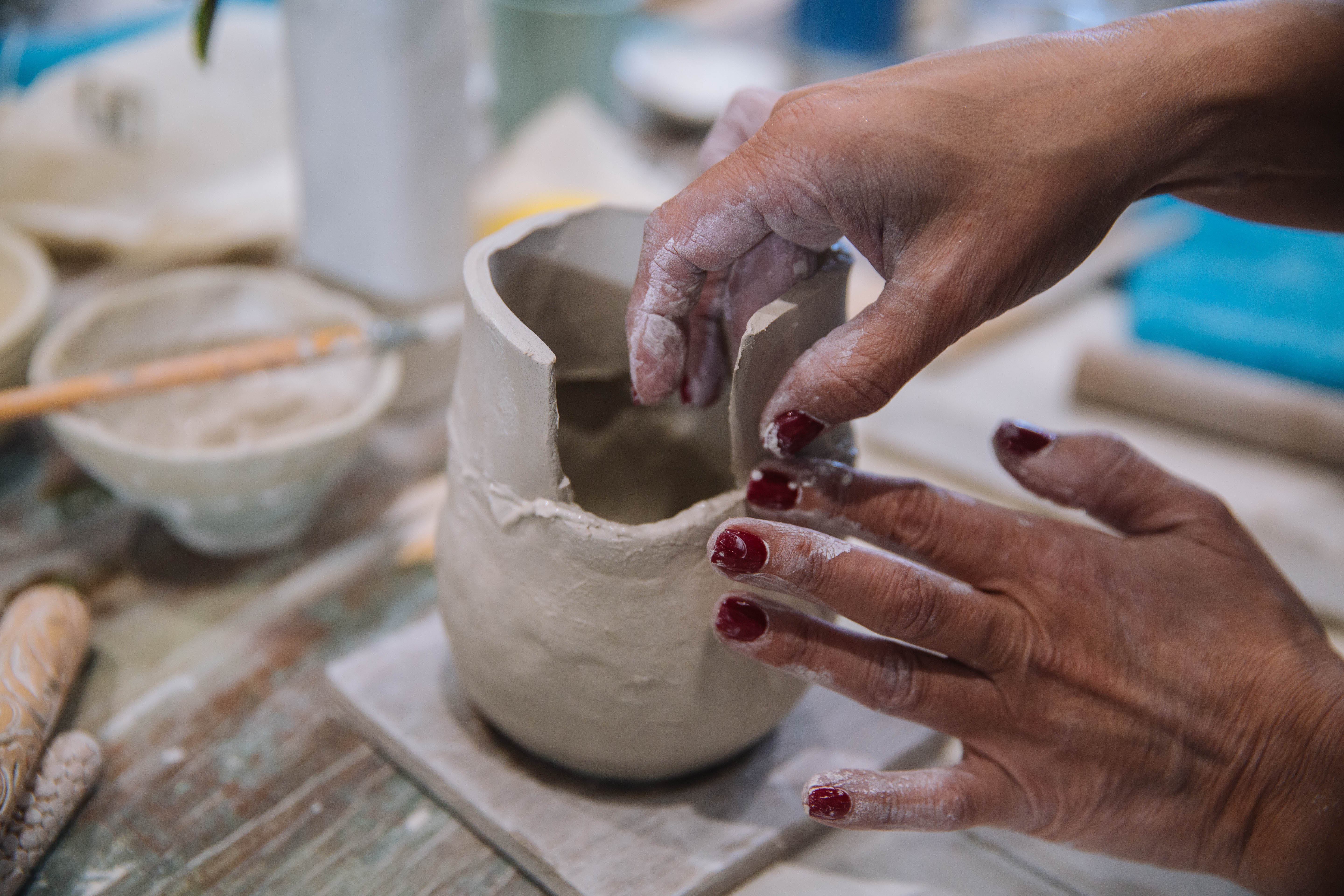 Close up of hands sculpting clay into a small vessel