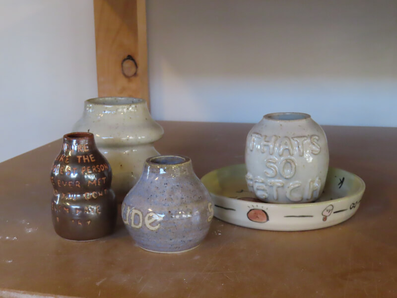 A selection of glazed handmade pottery sits on a wooden shelf