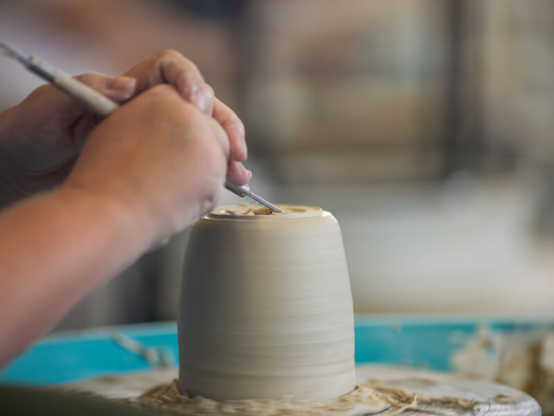Hands using a tool to shape clay on a potter's wheel