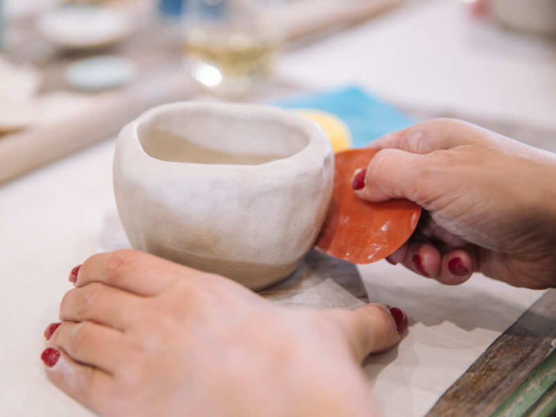 A close up of a person using a pottery tool to smooth the outside of a hand built pot