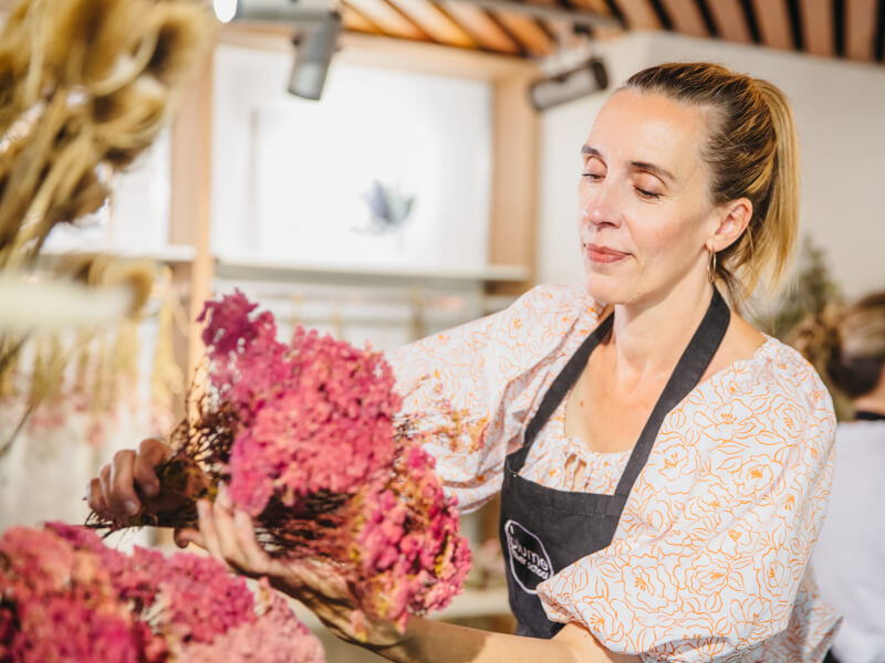 A woman is arranging a bouquet using large stems of pink flowers