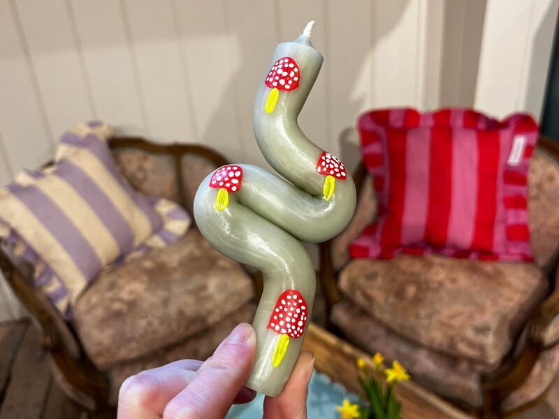 A close up of a hand holding a bendy green candle with toadstool designs painted on it in red and yellow