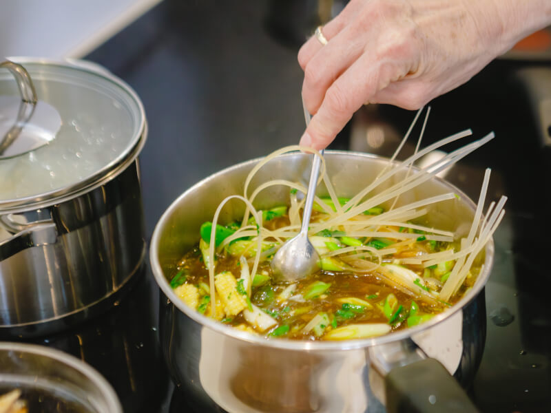 A close up of someone stirring a saucepan full of vegetables and sauce