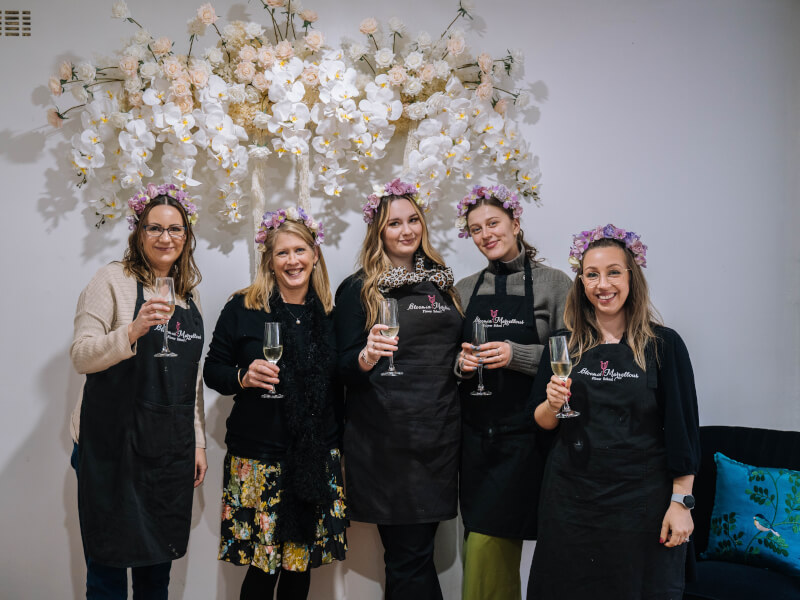 A group of women in flower crowns are smiling and holding champagne glasses