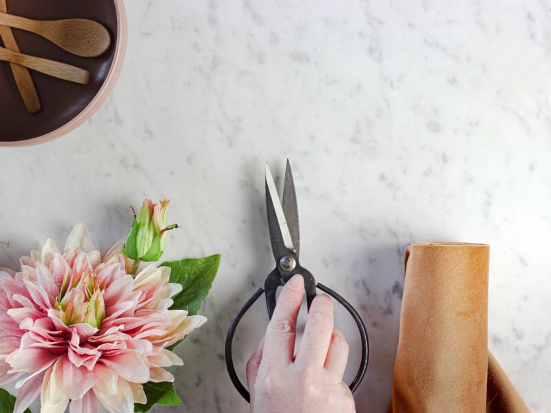 A person holding a pair of scissors next to a pink flower ready to create a floristry arrangement