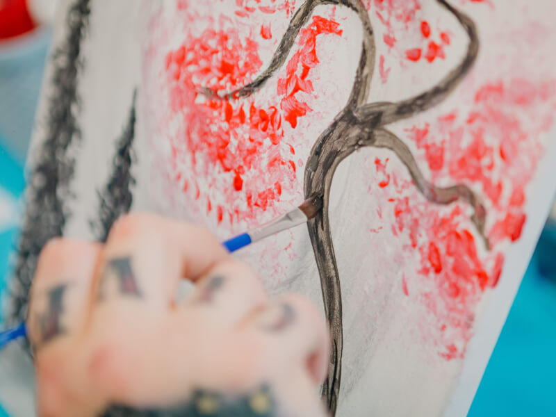 A painting of a brown tree trunk and branches with red blossom on a white background