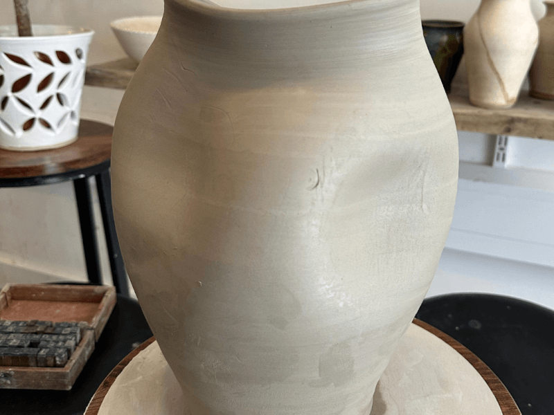 A large hug vase sitting on a wooden stool in a pottery studio