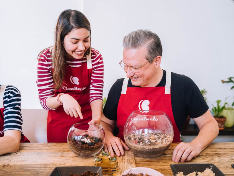 A woman and man are making glass terrariums at a wooden table