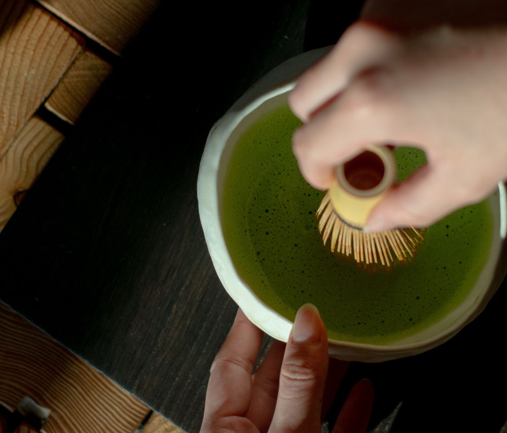 Hand whisking matcha in a bowl with a bamboo whisk