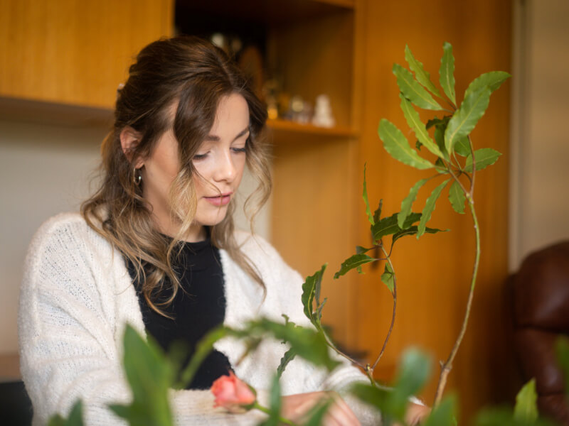 A woman is at an ikabana class, using a rose bush for flowers