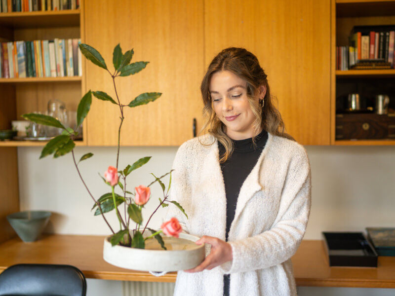 A woman holding a finished ikebana project made from a rose plant