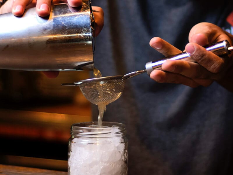 straining a cocktail into a glass jar