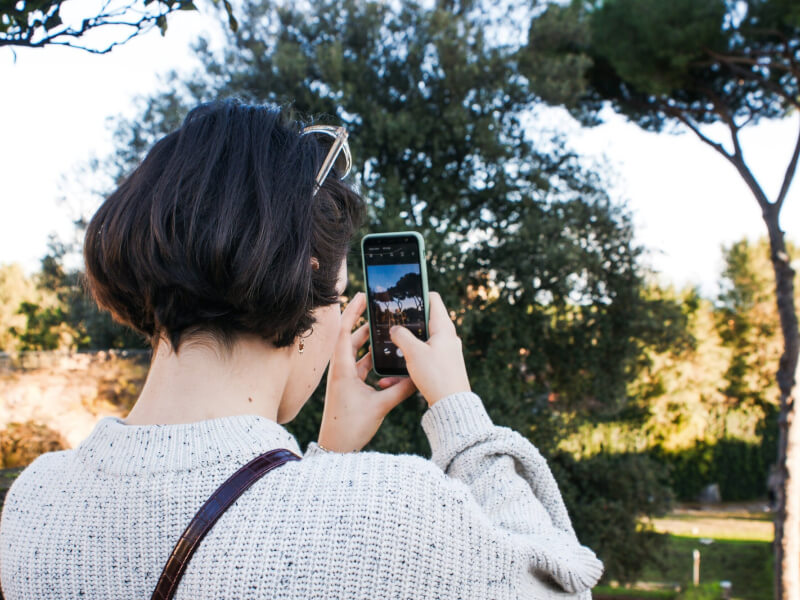 A woman is taking a picture of some trees with her smartphone