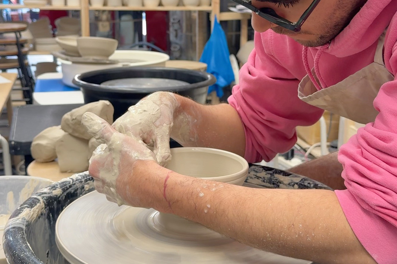 Close up of a man with glasses shaping clay on a pottery wheel