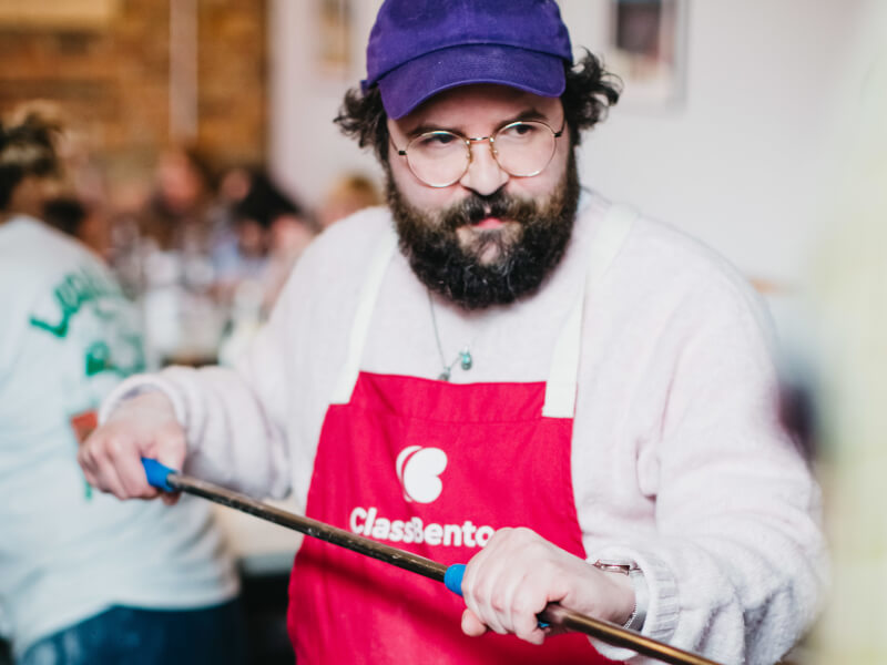 man in a purple hat working at a wood fired pizza oven
