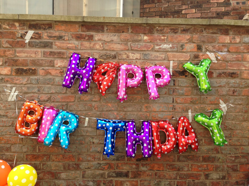 Happy Birthday letter balloons stuck to a brick wall for a virtual birthday party.