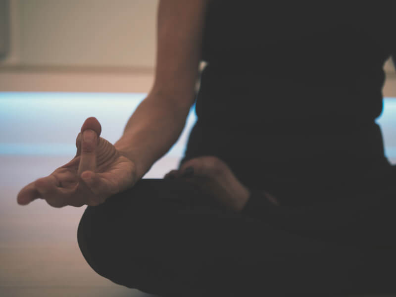 A person practicing sukhasana, a simple cross-legged yoga pose, at home.