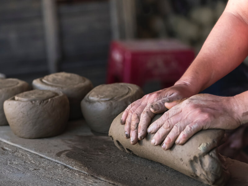 Hands pressing down on a roll of clay to make pottery at home.