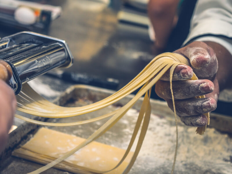 A person cutting homemade pasta with a pasta machine. 