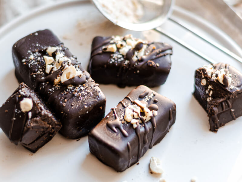 Some rectangular milk chocolates decorated with nuts and sugar are lying on a white plate 